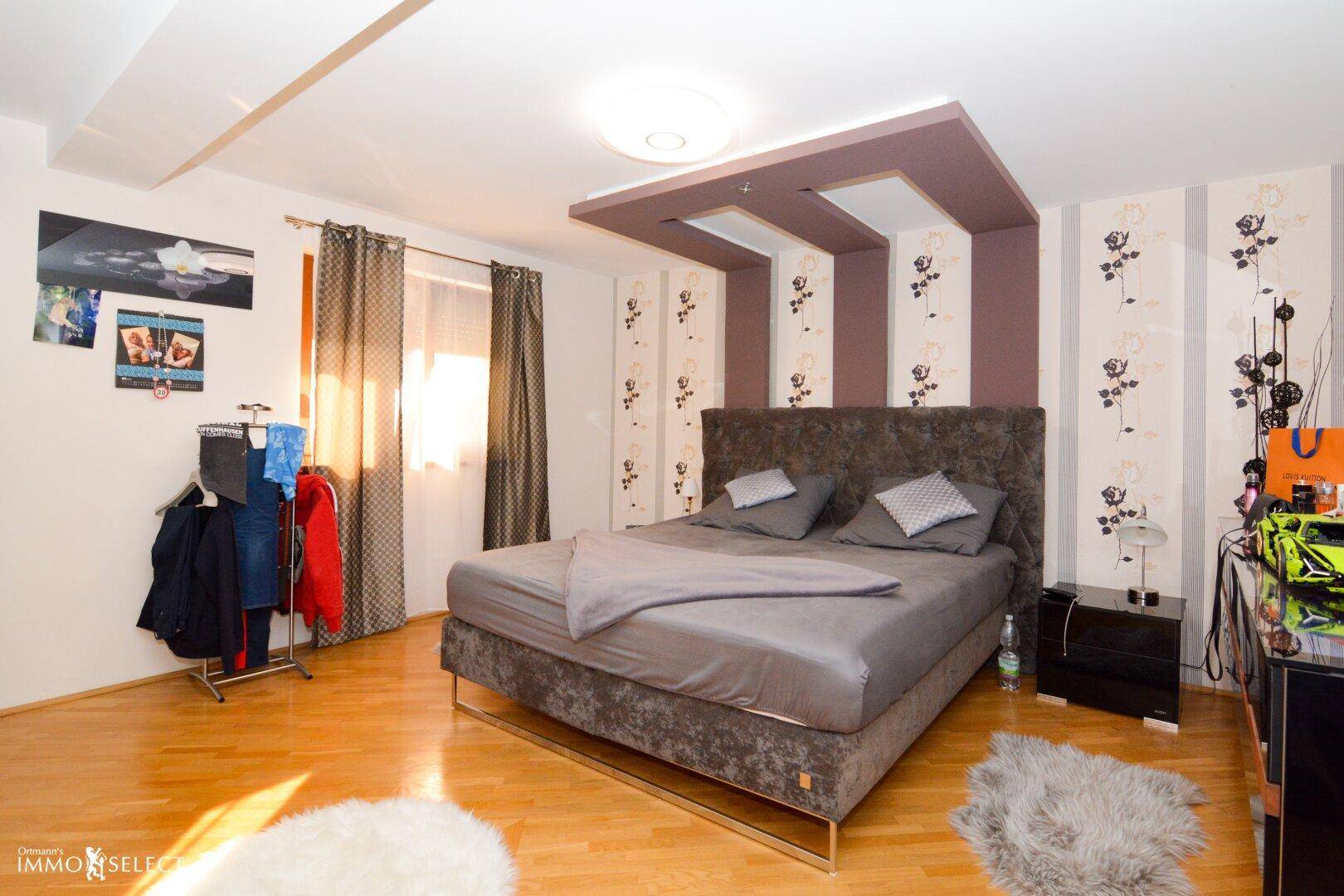 Schlafzimmer mit Holzboden, großem Bett und dekorativer Deckenbeleuchtung.