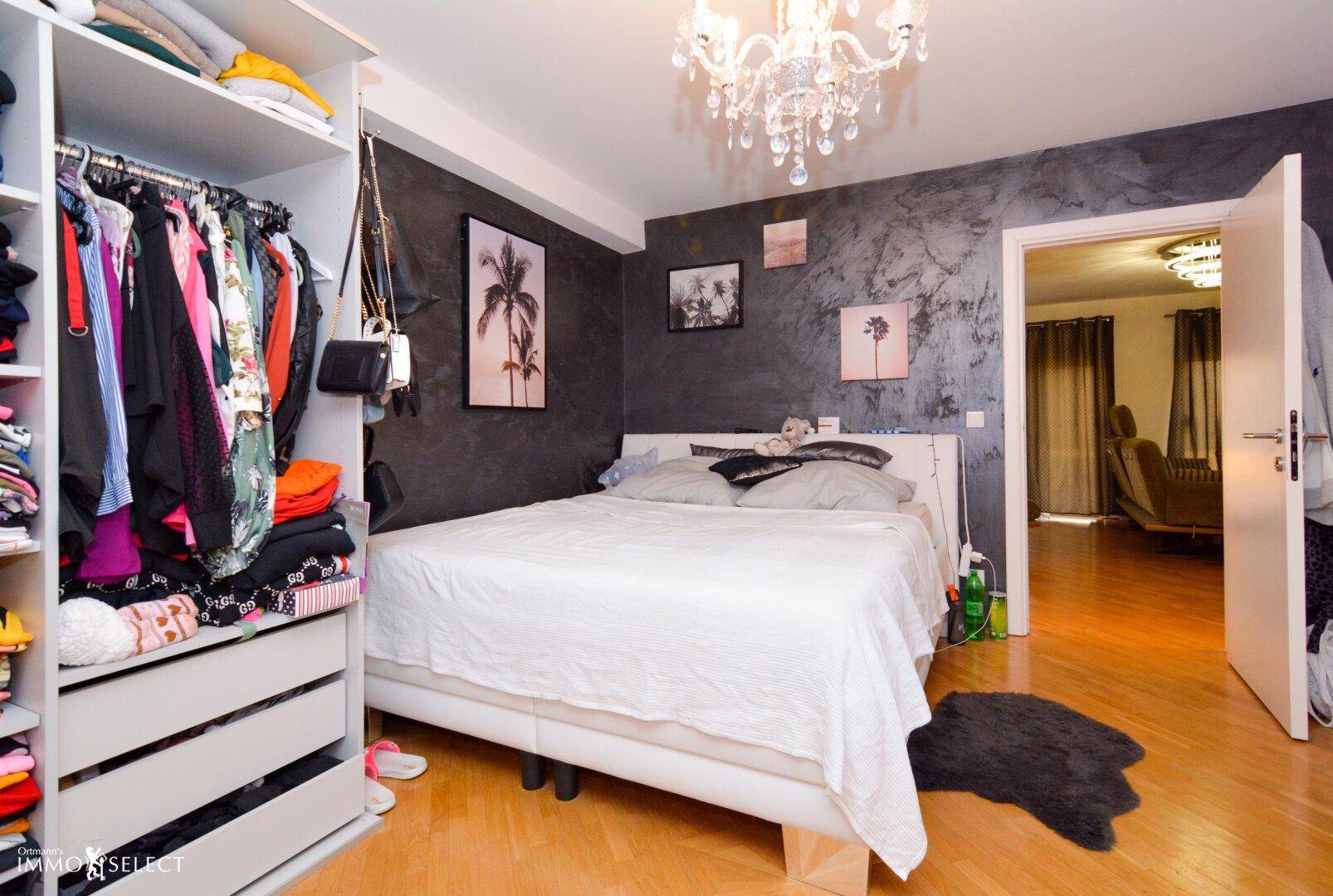Schlafzimmer mit Holzboden, großem Bett, Kleiderschrank und dunkler Akzentwand.