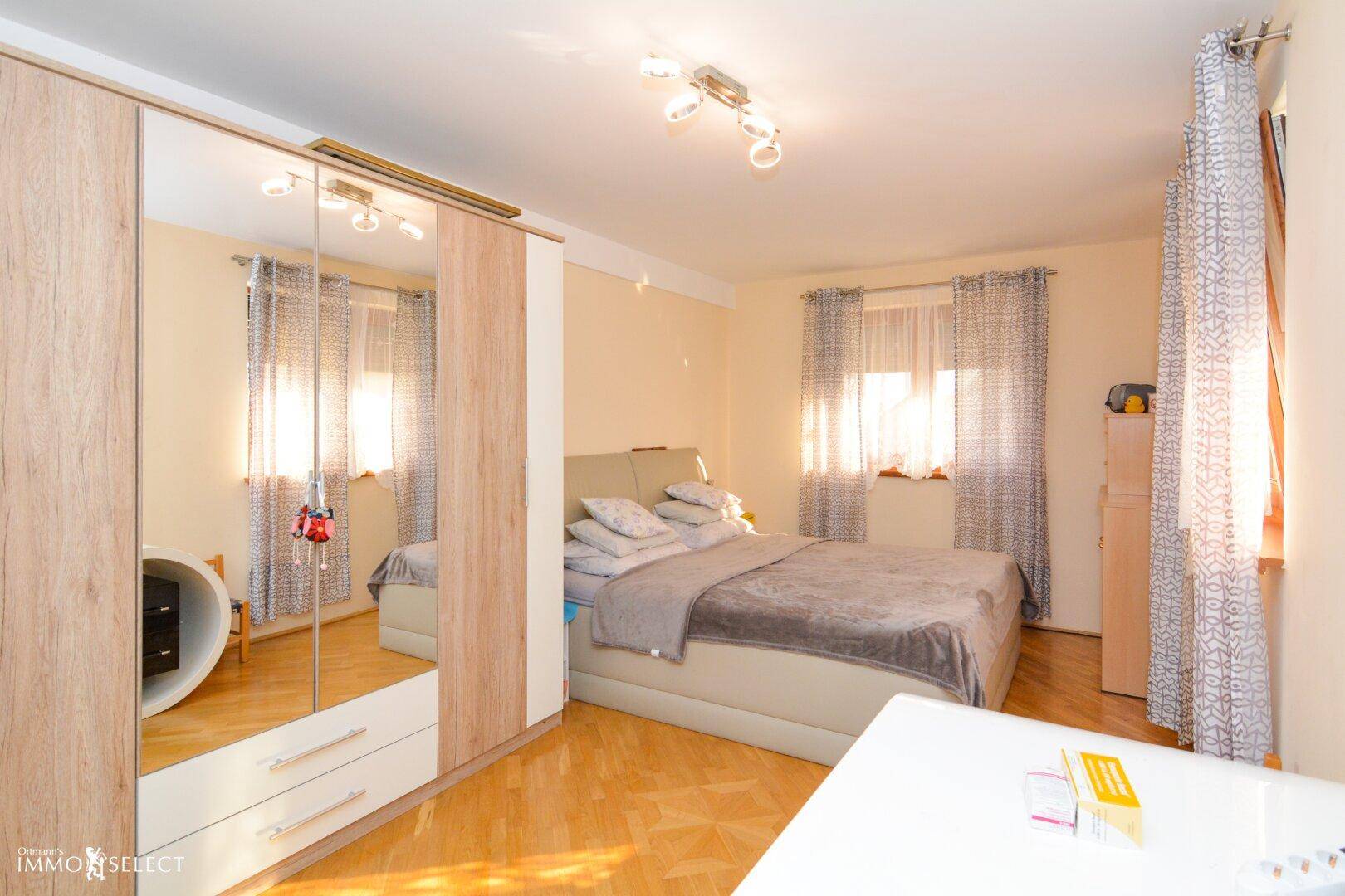 Helles Schlafzimmer mit Holzboden, großem Bett und Spiegelschrank.