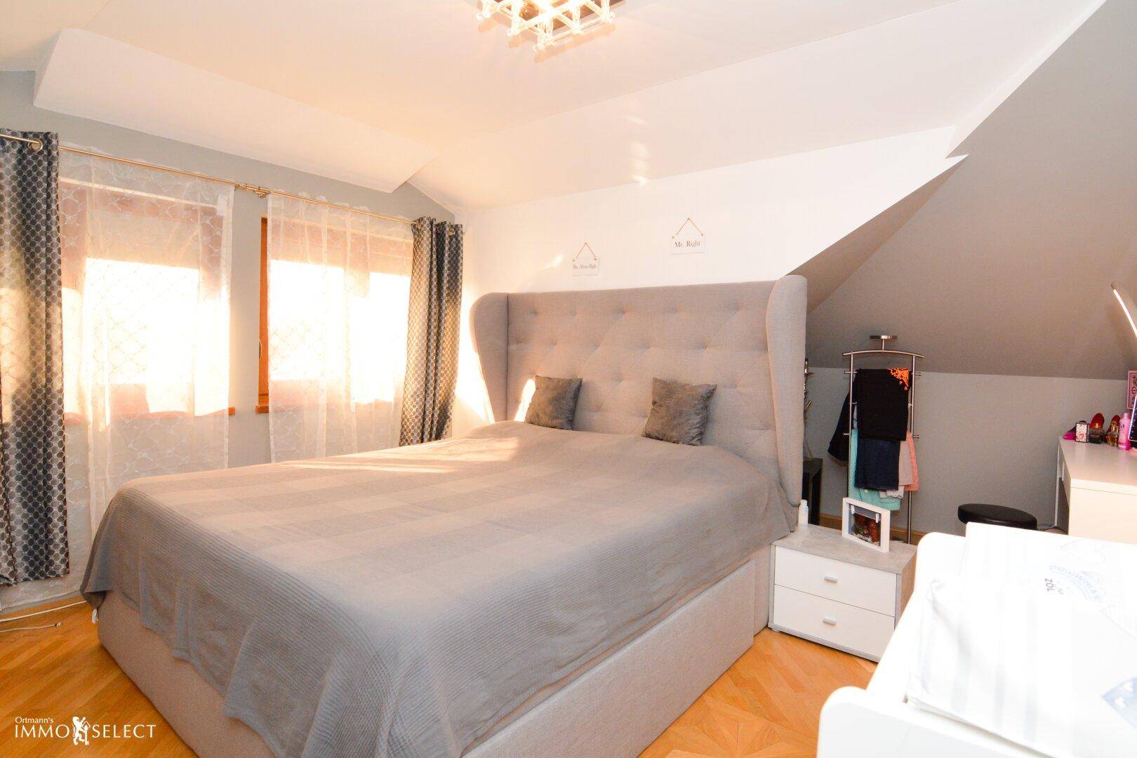 Helles Schlafzimmer mit Holzboden, großem Bett und Dachschräge.