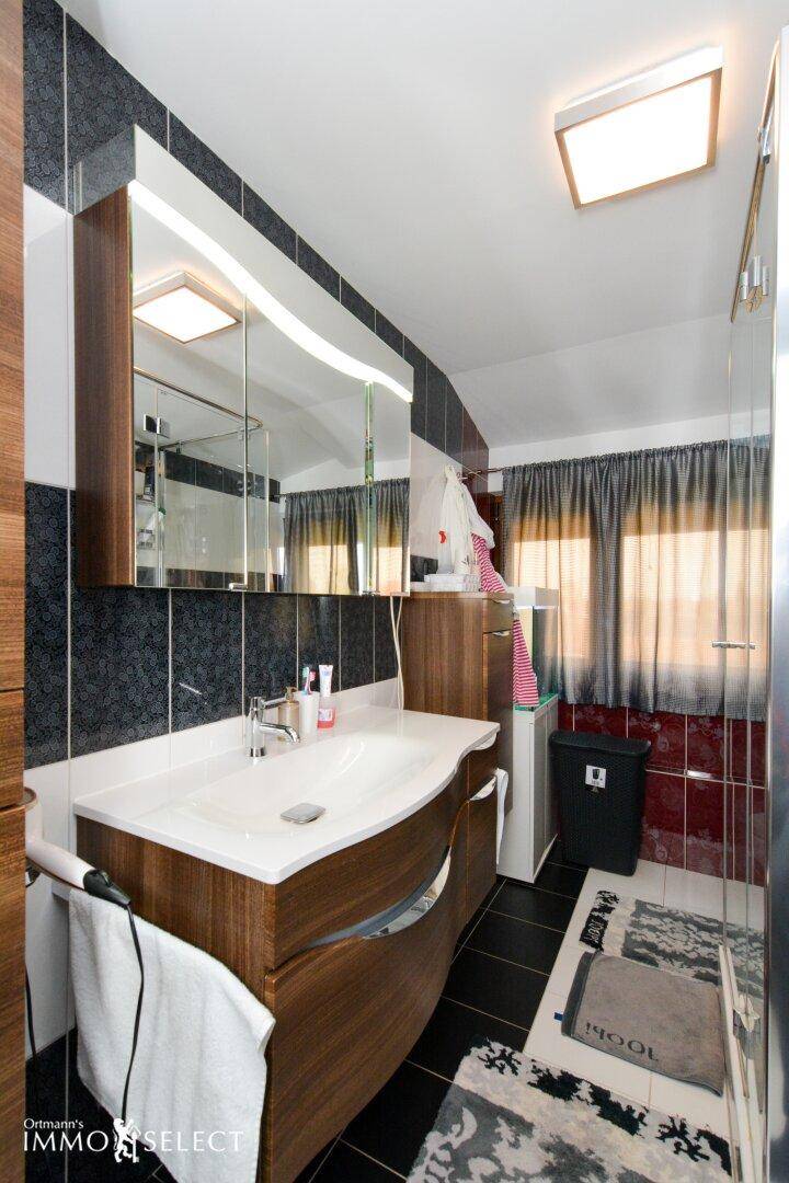 Modernes Badezimmer mit dunklen Fliesen, Holzwaschtisch und Spiegelschrank.