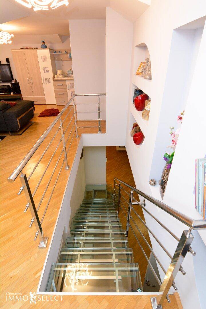 Heller Flur mit Holzboden und moderner Glas-Edelstahl-Treppe zum Untergeschoss.