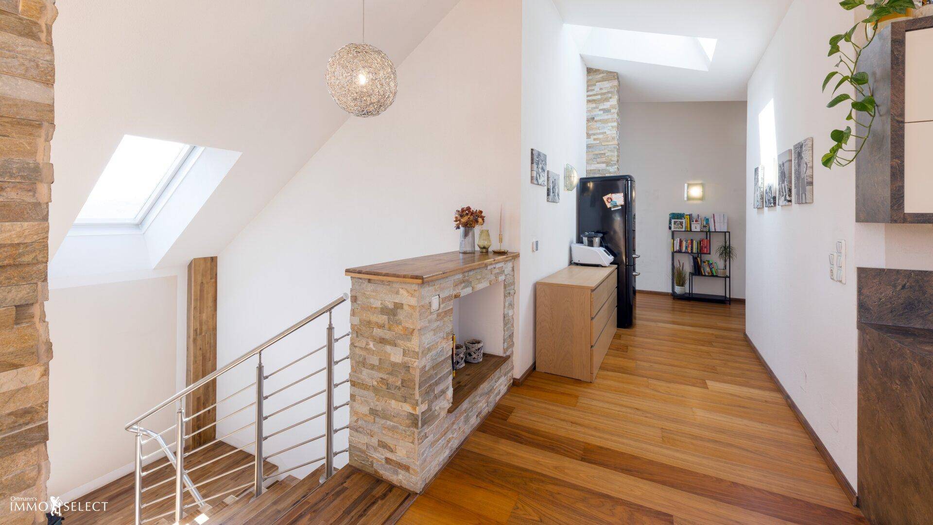 Heller Flur mit Holztreppe, Steinverkleidung und Dachfenster im Obergeschoss.