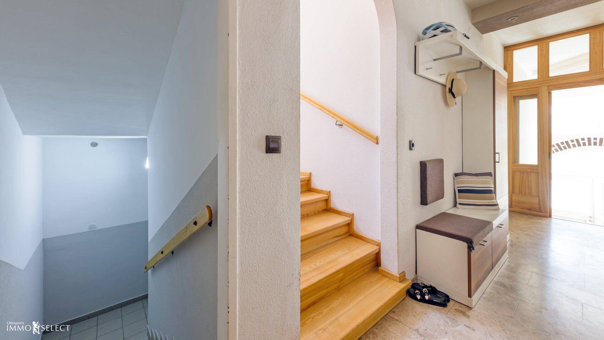 Eingangsbereich mit Garderobe und Holztreppe, die zum Obergeschoss führt.