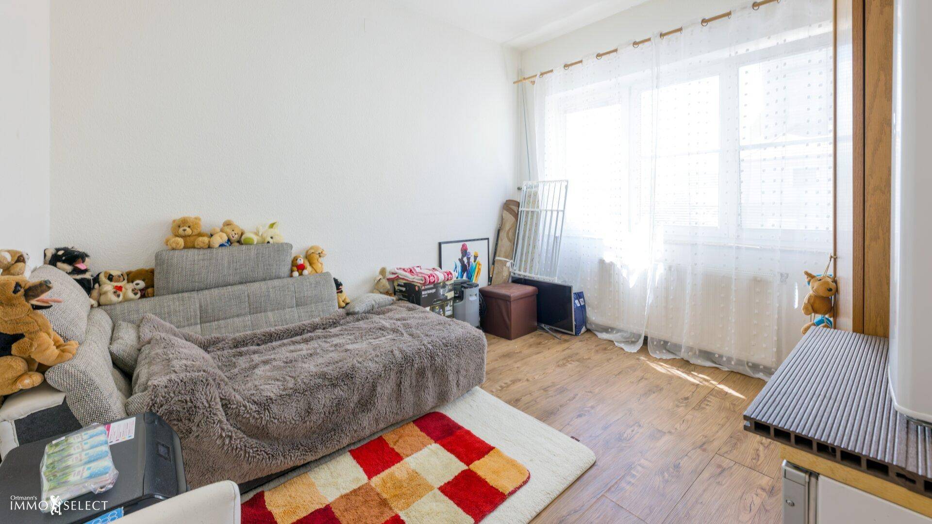 Helles Wohnzimmer mit großem Fenster, Holzboden und gemütlicher Einrichtung, einladend und geräumig.
