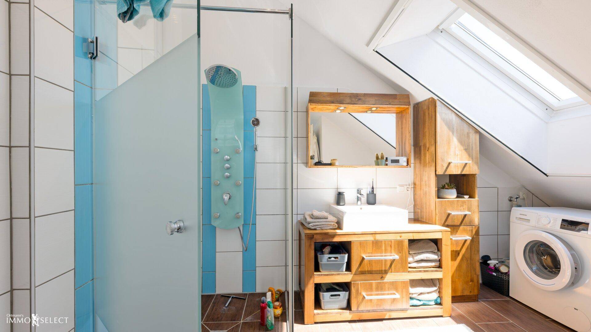Geräumiges Badezimmer mit Dusche, Waschmaschine und Dachfenster im Dachgeschoss.