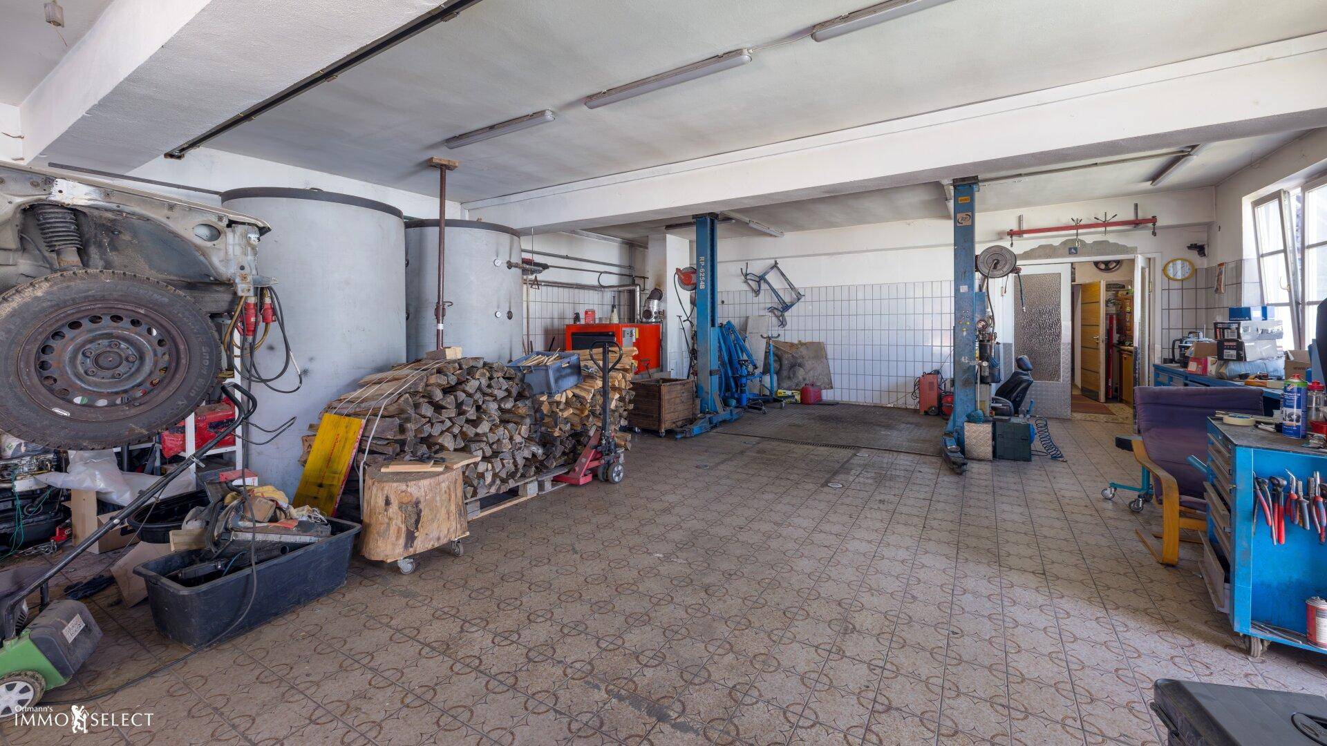 Große Garage mit Hebebühne, Werkzeugen und Holzstapel, ideal für Fahrzeuge und Handwerk.