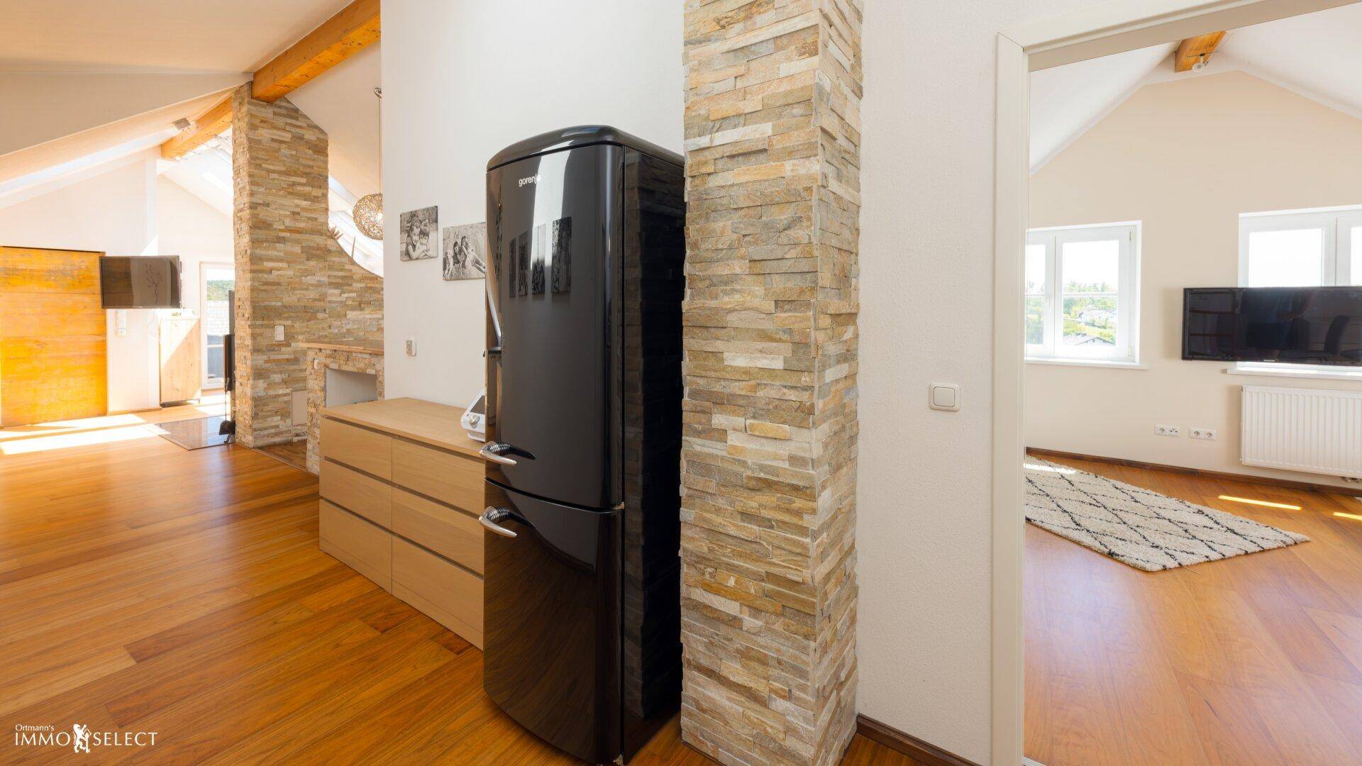 Offener Wohnbereich mit Holzboden, Steinverkleidung und modernem Kühlschrank.