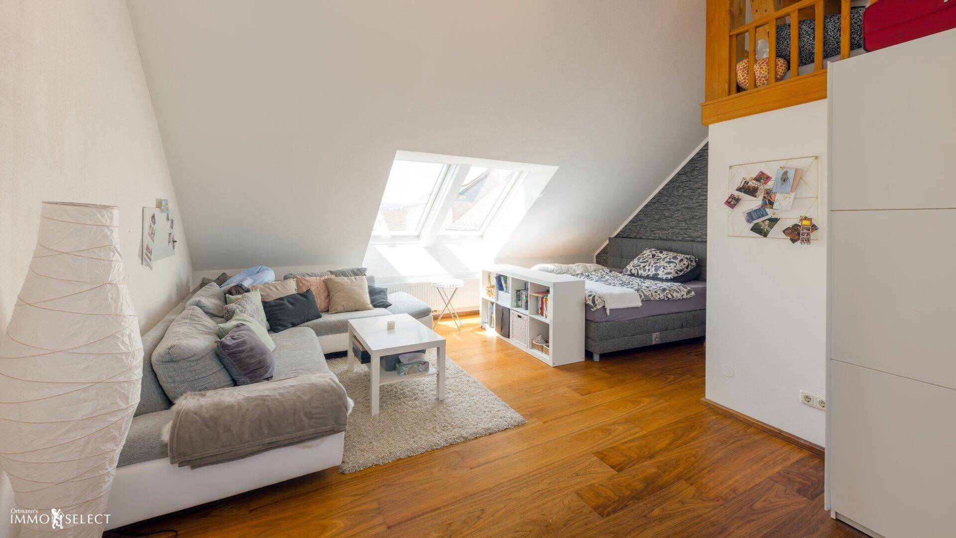 Gemütlicher Wohnbereich im Dachgeschoss mit Schrägdach, Sofa und Holzboden, hell durch Dachfenster.