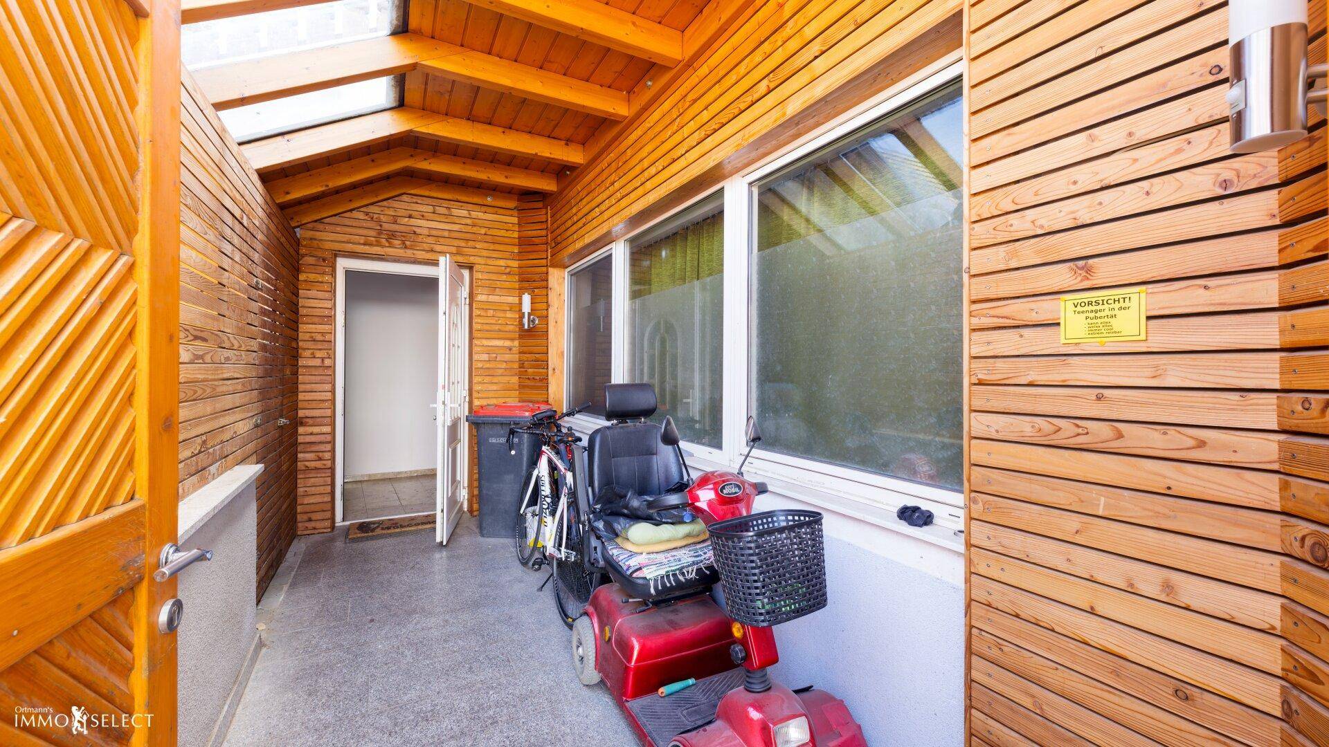Überdachter Eingangsbereich mit Holzverkleidung und Abstellmöglichkeiten, praktisch und geschützt.
