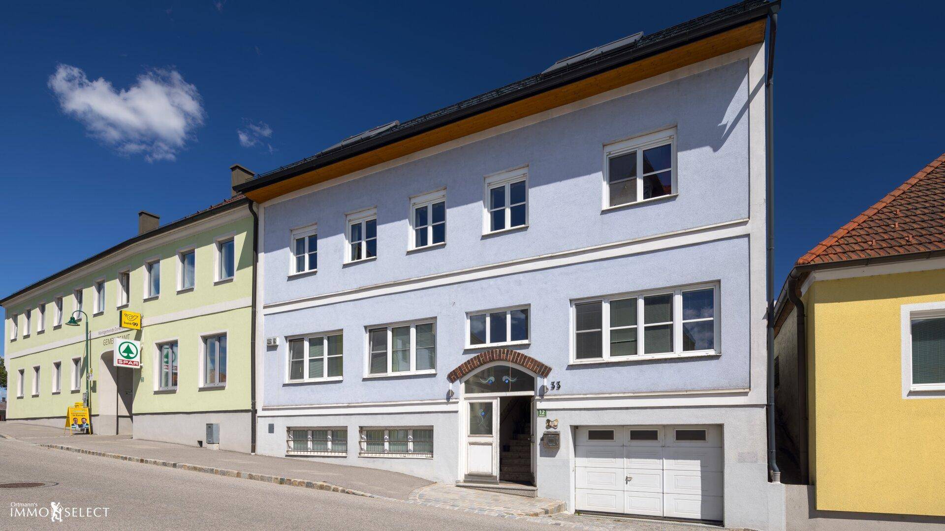 Fassade eines Mehrfamilienhauses mit hellblauer Farbe und Garageneinfahrt, gut gepflegt und einladend.