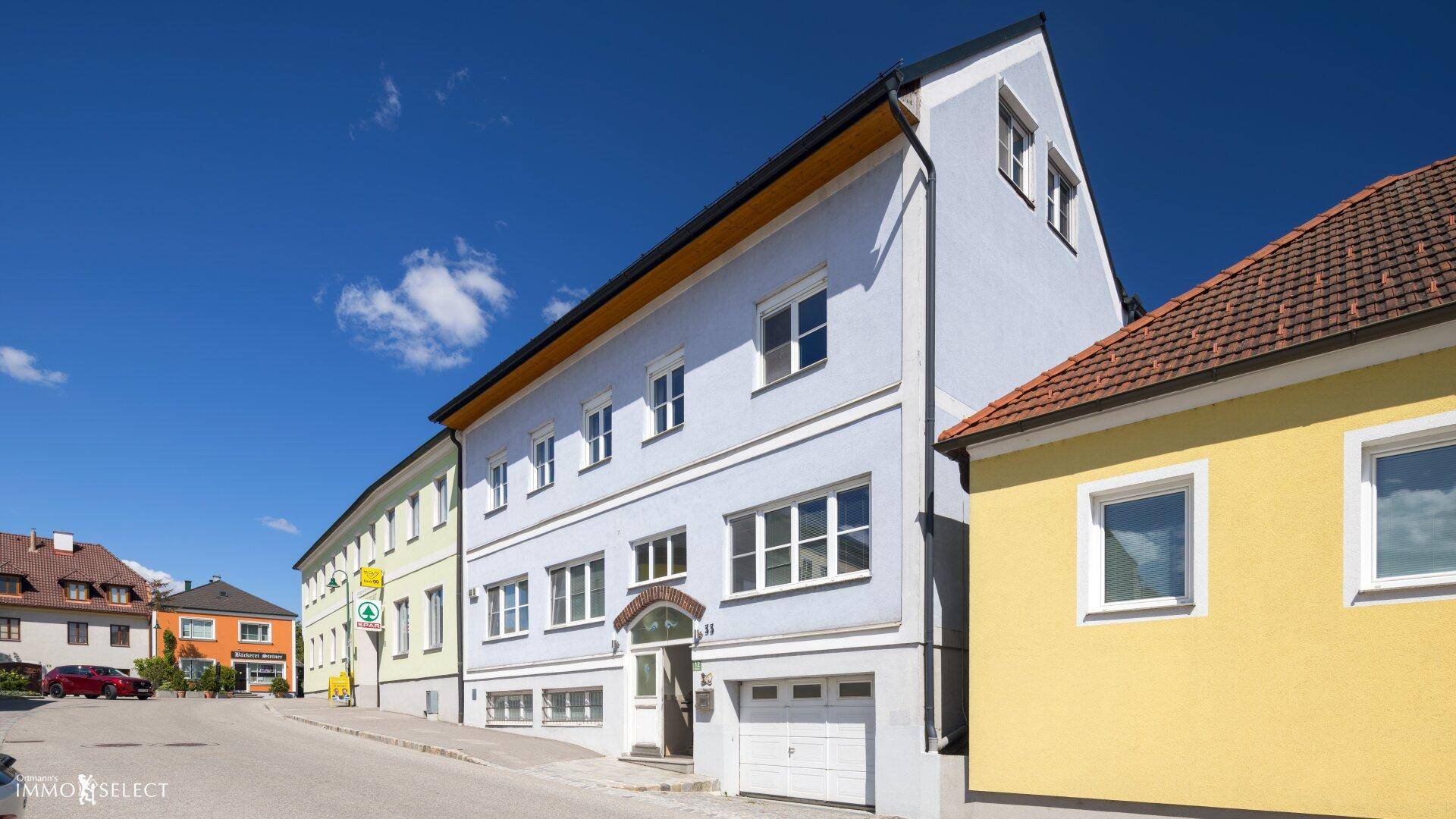 Ansicht der Gebäudefassade von der Straße mit blauer Farbe und Garagentor, in einer städtischen Umgebung.