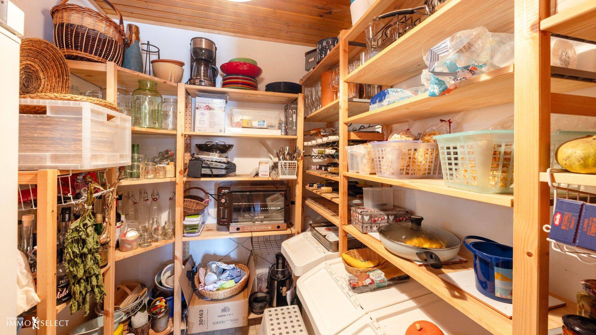 Gut organisierte Speisekammer mit vielen Holzregalen und reichlich Vorräten für den Haushalt.