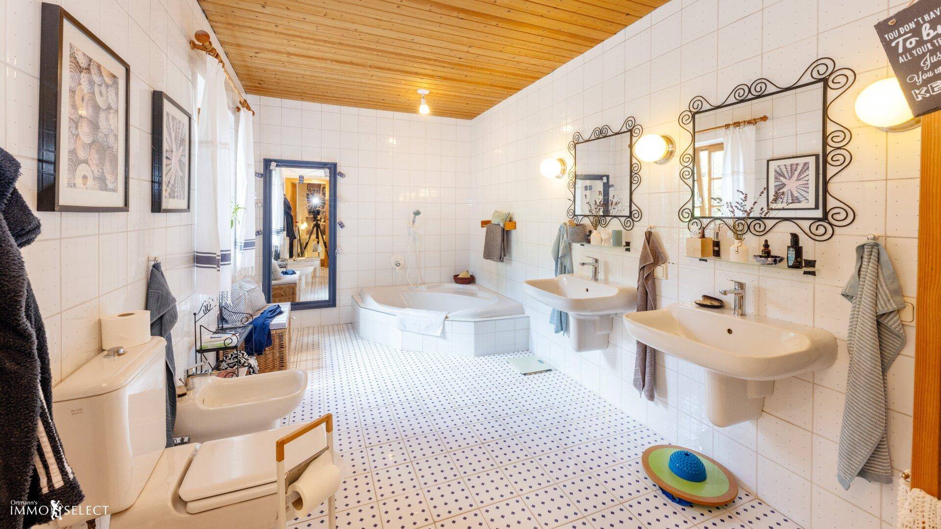 Helles Badezimmer mit Eckbadewanne, Doppelwaschbecken und klassischen weißen Fliesen.