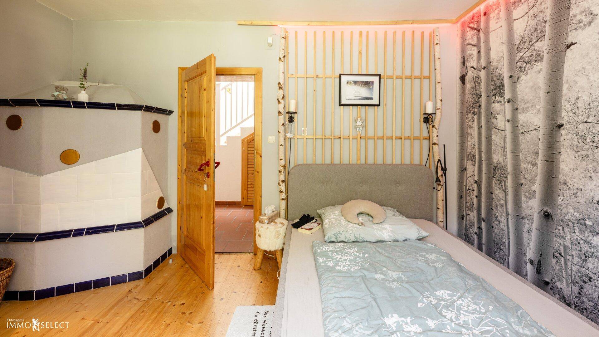 Schlafzimmer mit Holzboden, einem traditionellen Kachelofen und direktem Zugang zum Treppenhaus.