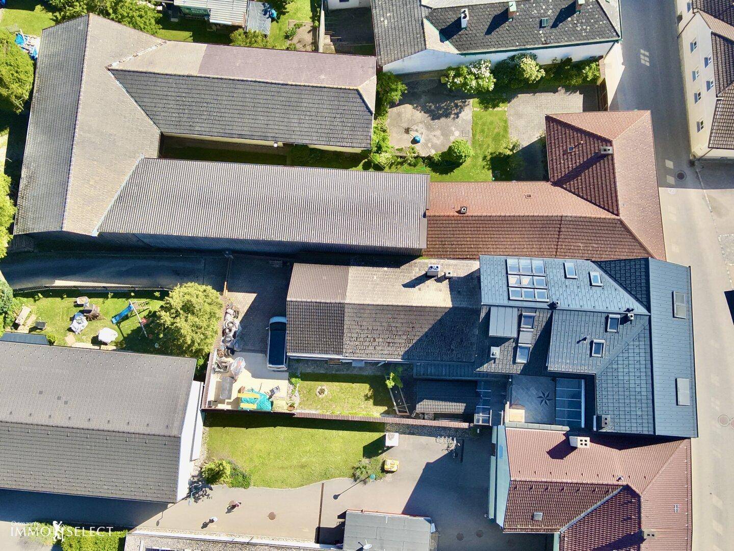Luftaufnahme eines Wohngebiets mit mehreren Häusern, Gärten und Dächern in verschiedenen Farben.