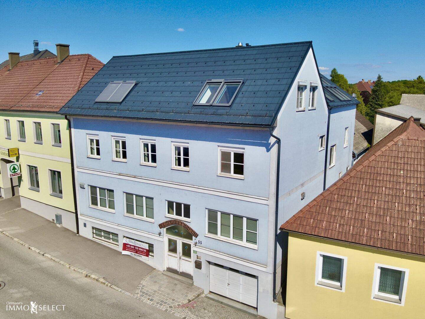 Ansicht der hellblauen Gebäudefassade mit vielen Fenstern und einem modernen Dach mit Dachfenstern.