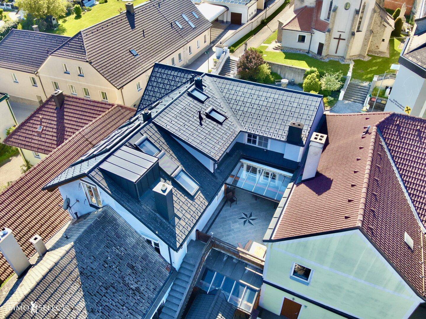 Dachansicht des Gebäudes mit mehreren Dachfenstern und einem Innenhof mit Sitzgelegenheiten und einem Sternmuster.