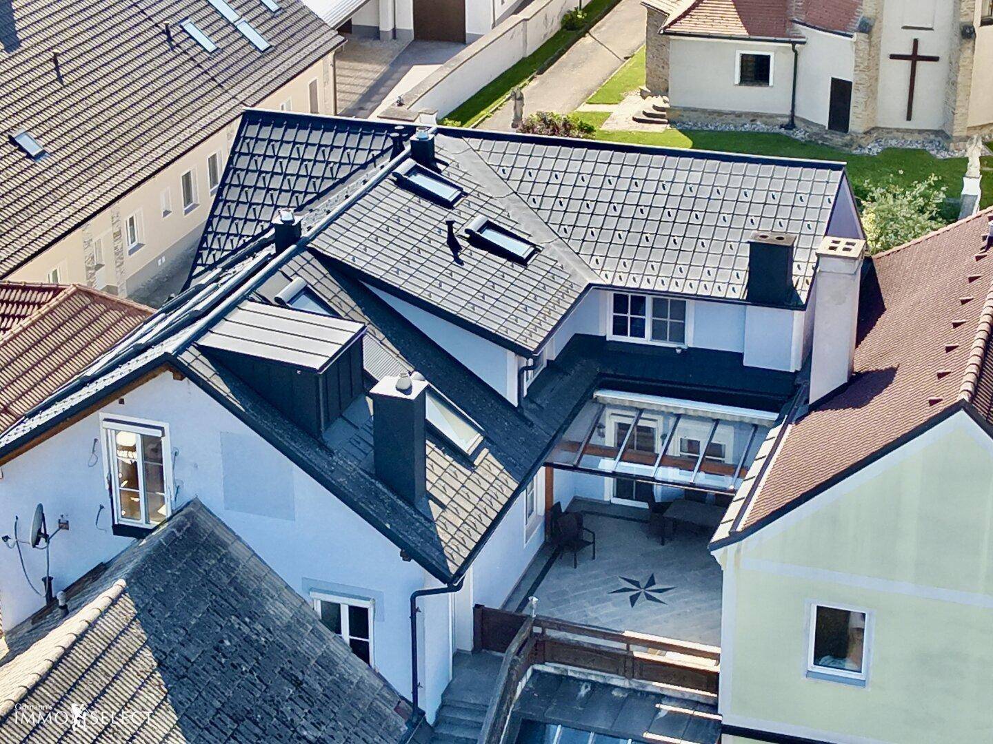 Nahaufnahme der Dächer mit Dachfenstern und einem gepflasterten Innenhof mit Sitzmöbeln.