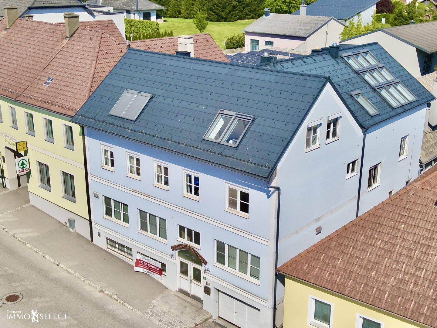 Ansicht der hellblauen Gebäudefassade mit mehreren Fenstern und einem modernen Dach mit Dachfenstern.