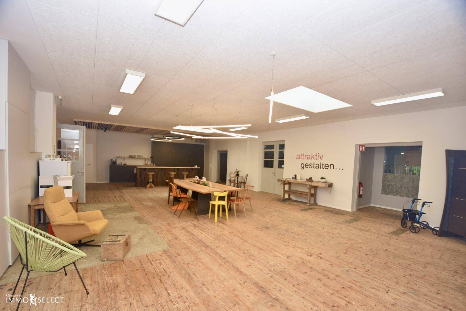 Großer offener Raum mit Holzboden, Essbereich, Lounge-Möbeln und einer modernen Küchenzeile im Hintergrund.