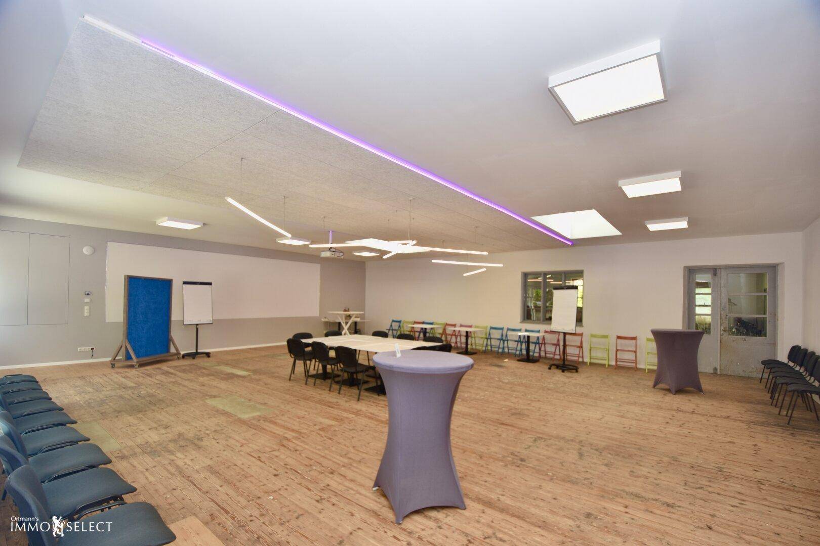 Großer Konferenzraum mit Holzboden, flexibler Bestuhlung und moderner Deckenbeleuchtung für Veranstaltungen.
