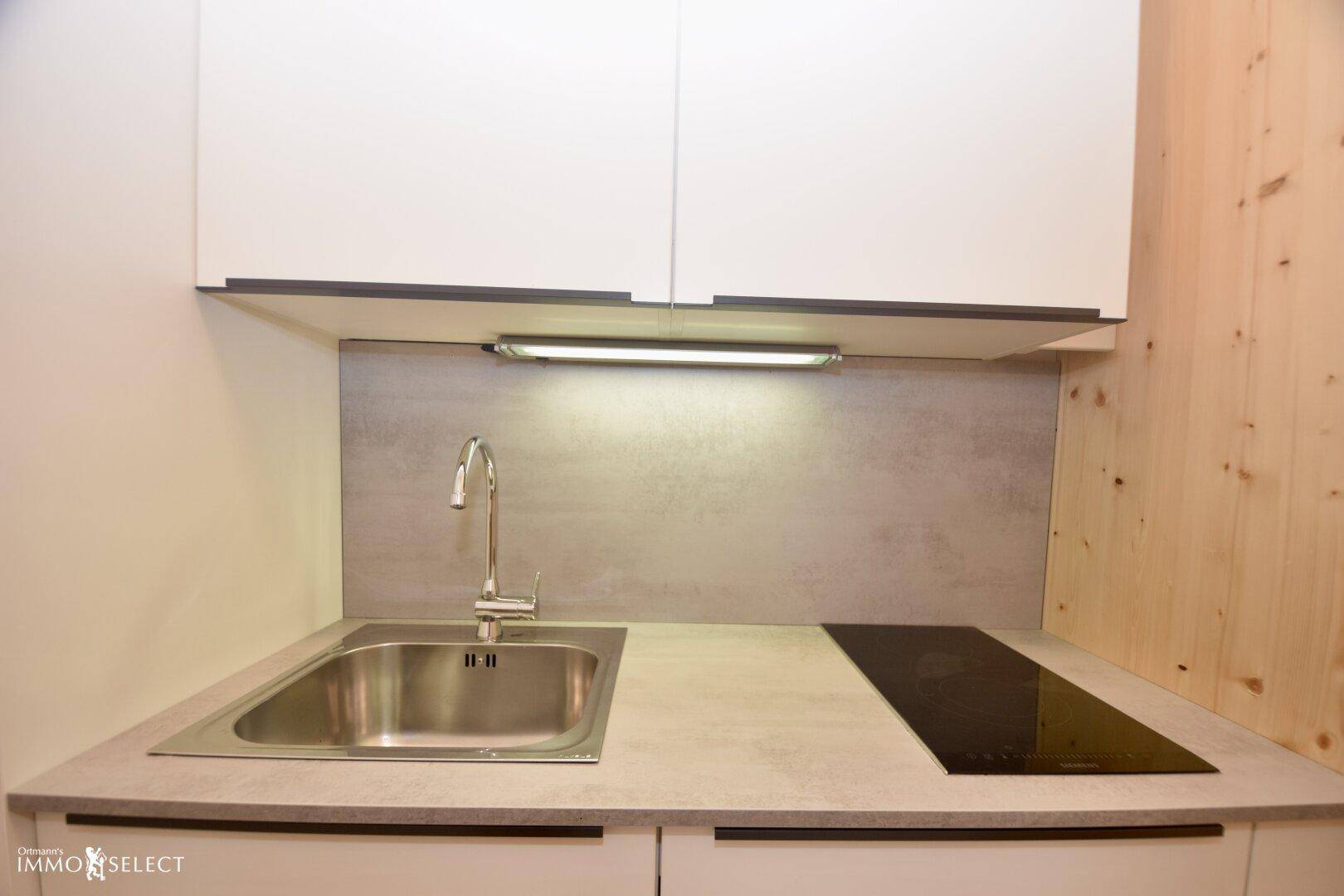 Kleine, moderne Küchenzeile mit Spüle, Induktionskochfeld und weißen Oberschränken.