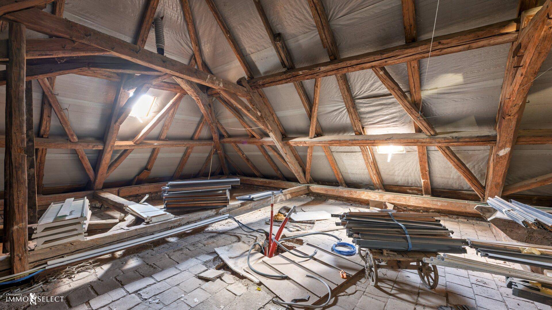 Dachboden mit sichtbarer Holzkonstruktion, Isolierung und natürlichem Lichteinfall durch Dachfenster.