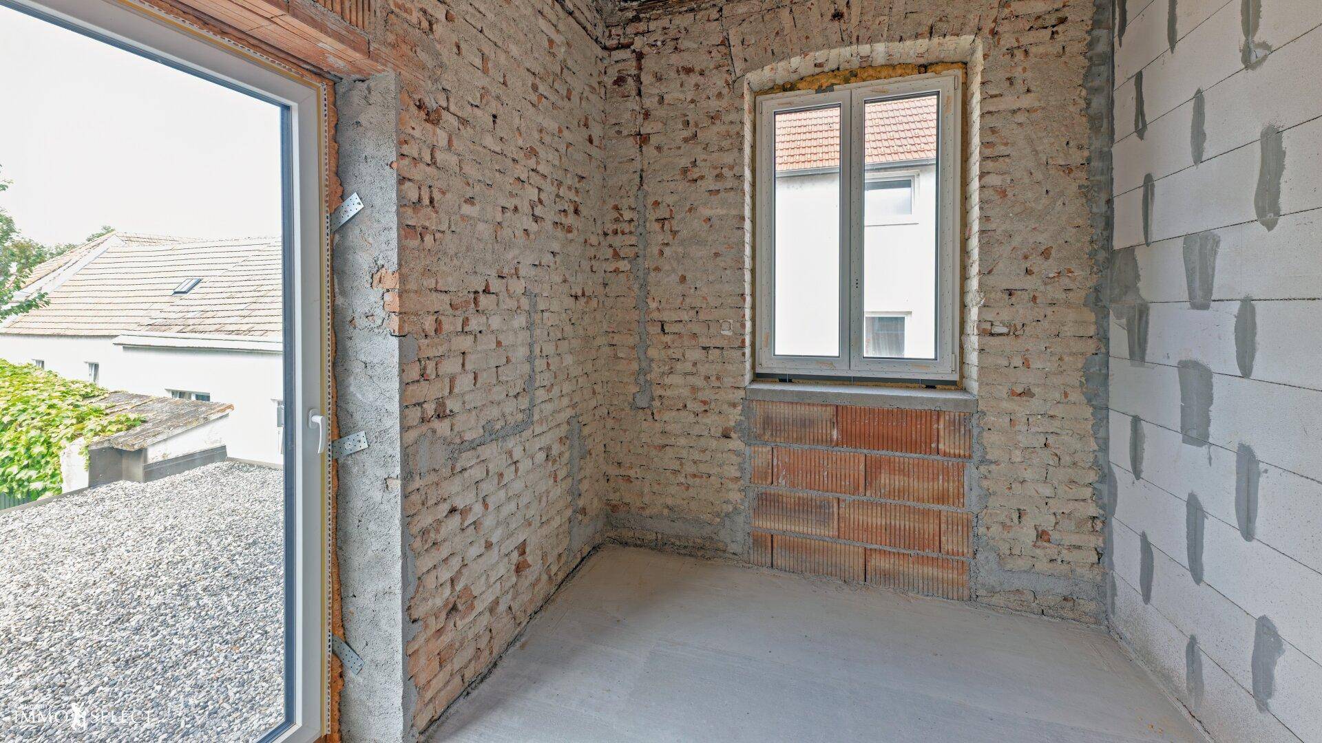 Raum im Rohbau mit unverputzten Ziegelwänden, Betonboden und neuen Fenstern.