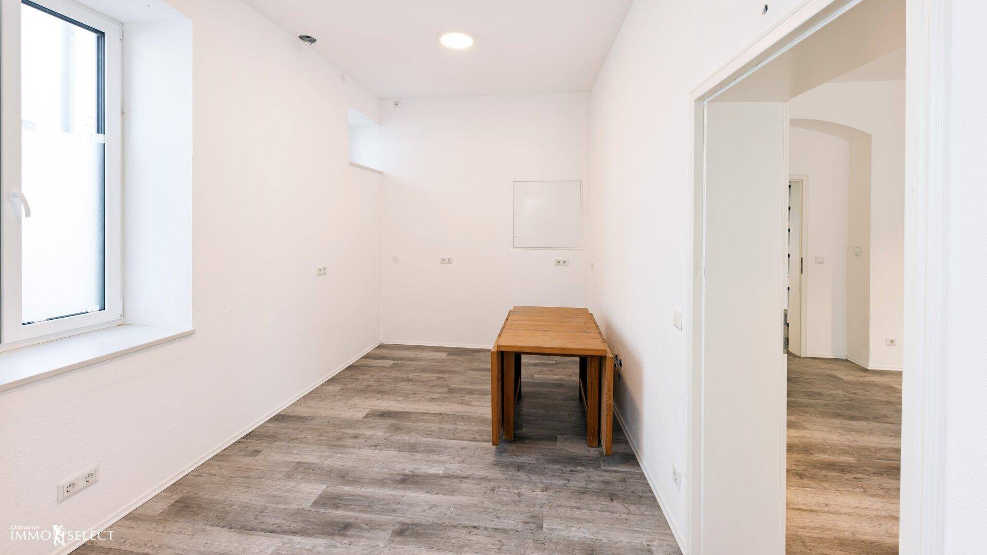 Heller Raum mit modernem Laminatboden, weißen Wänden und einem Holztisch.
