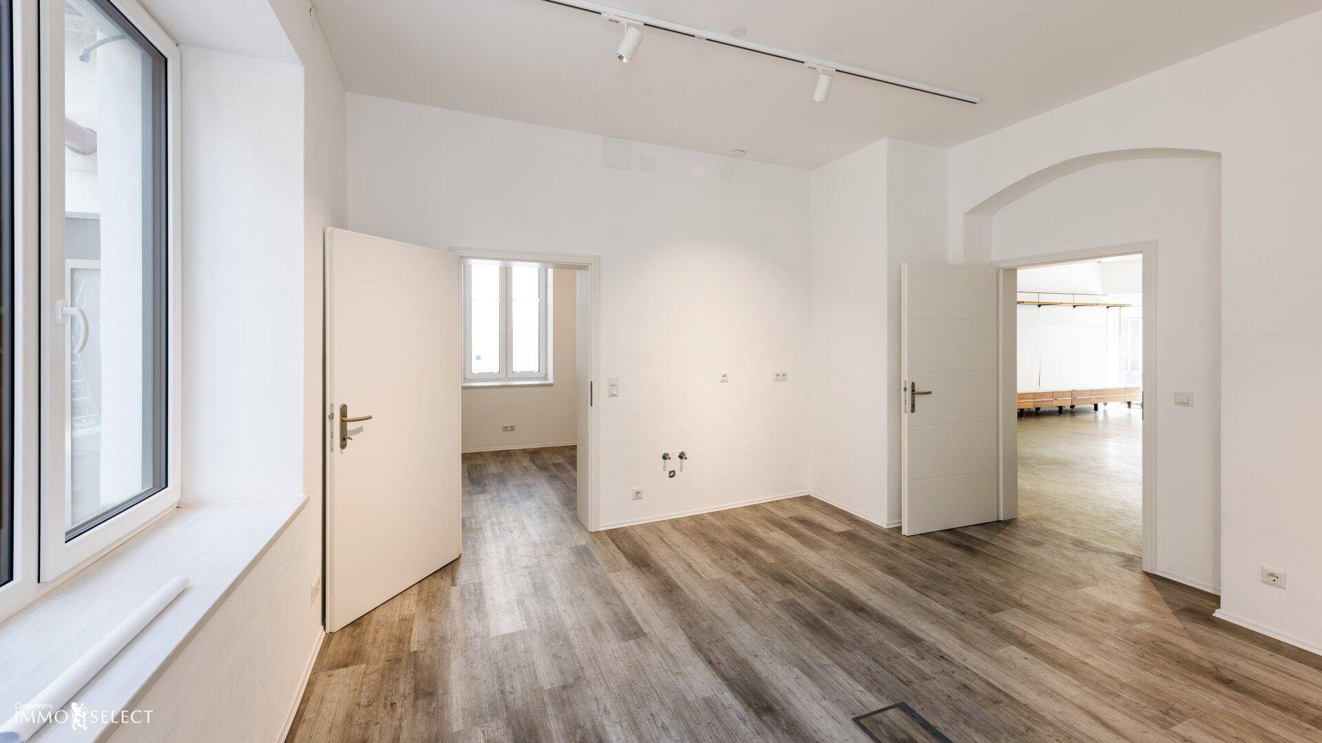 Heller Raum mit modernem Laminatboden, weißen Wänden und mehreren Türen zu angrenzenden Räumen.
