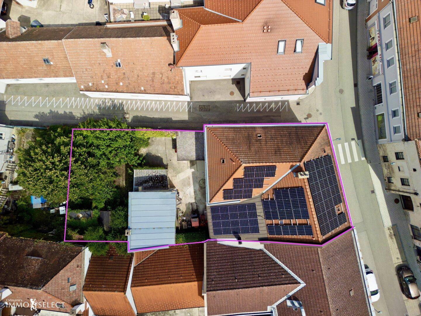 Luftaufnahme eines Gebäudes mit Solaranlagen auf dem Dach und angrenzendem Gartenbereich.