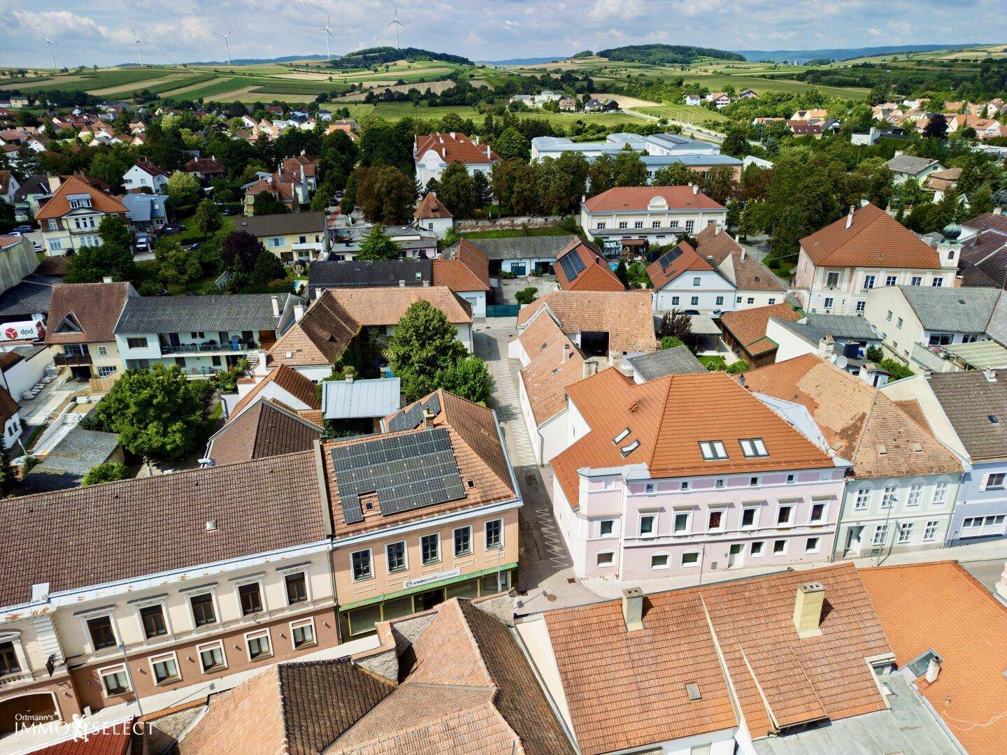 Weitläufige Luftaufnahme einer Stadt mit vielen Häusern und grünen Hügeln im Hintergrund.