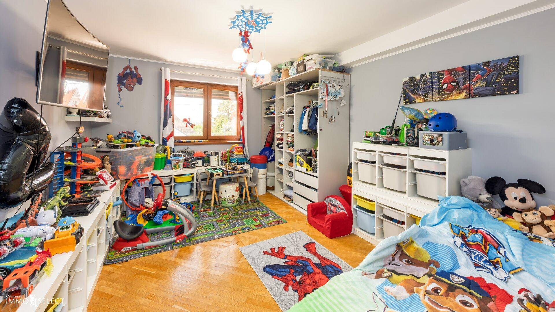 Kinderzimmer mit Holzboden, Spielzeug und bunten Dekorationen.