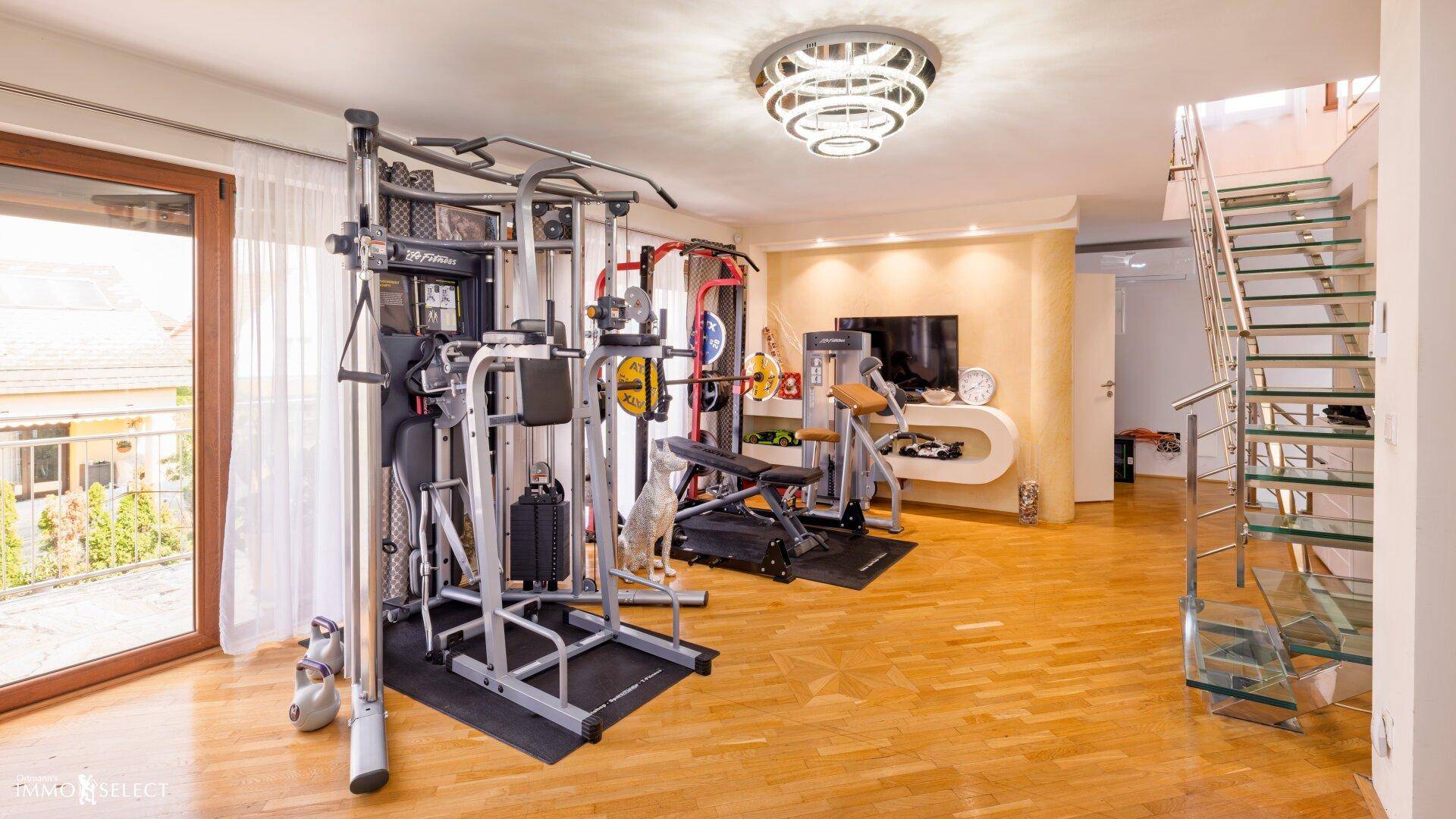 Geräumiger Fitnessraum mit verschiedenen Trainingsgeräten und Zugang zur Terrasse.