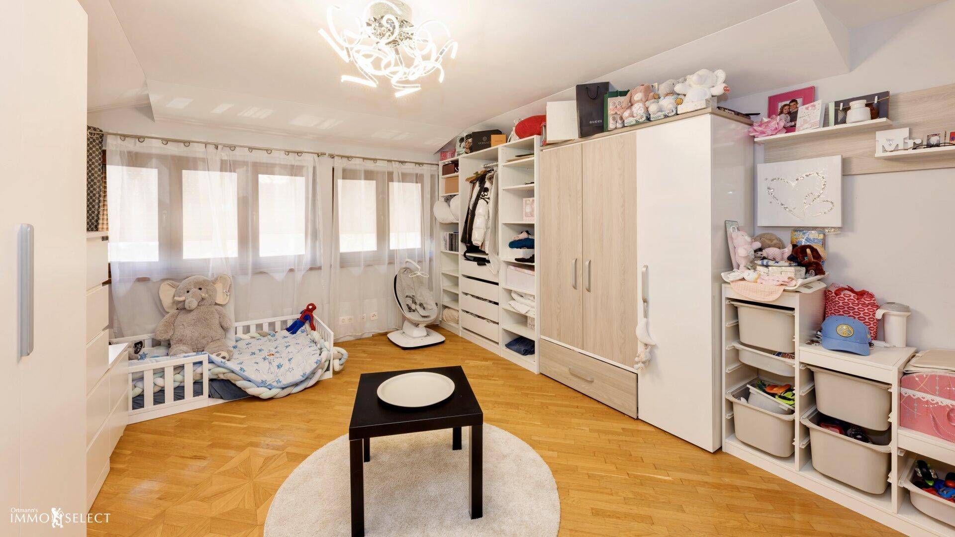 Helles Zimmer mit Parkettboden, großem Kleiderschrank und Babybett, ideal als Kinderzimmer.