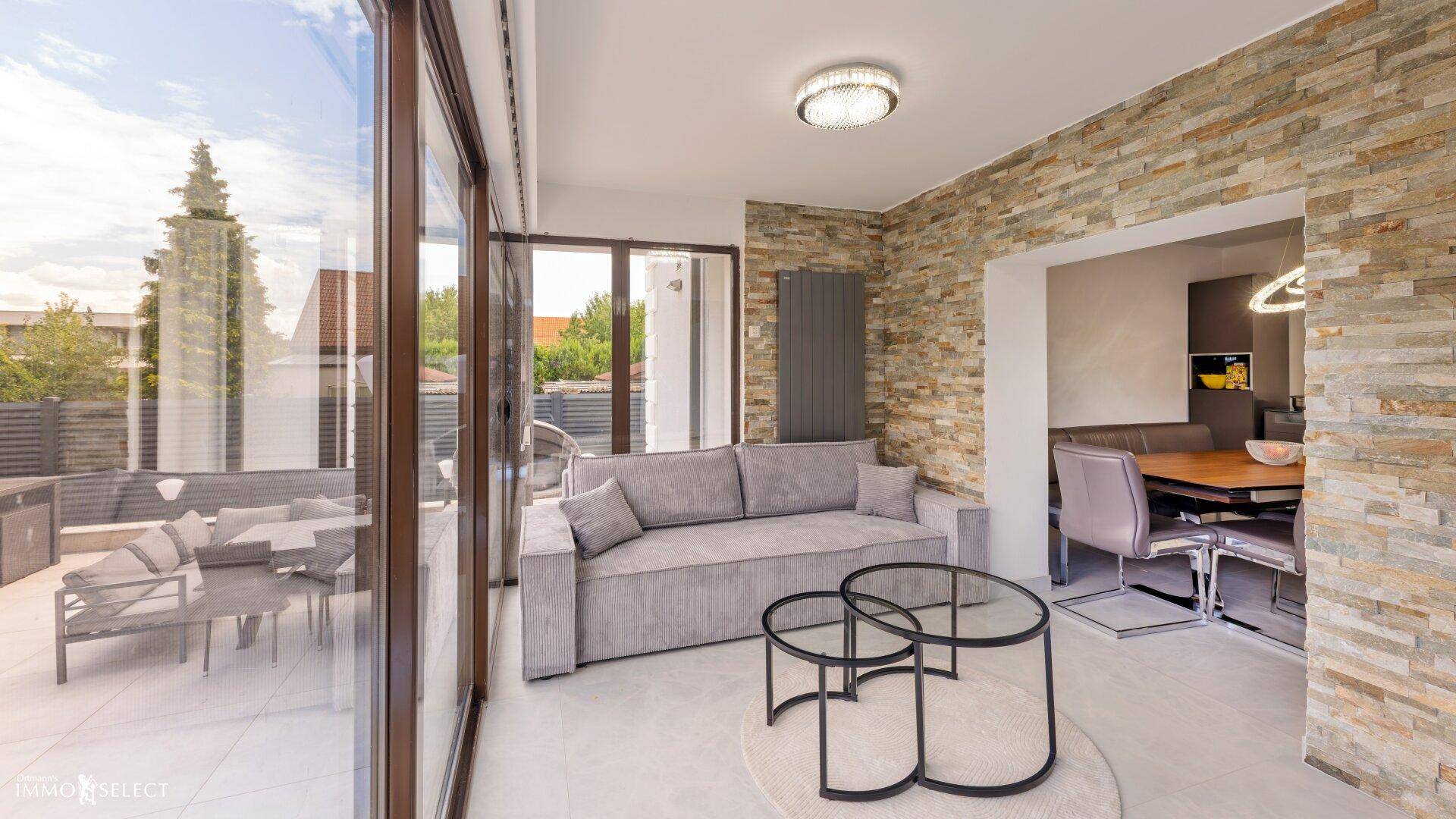 Modernes Wohnzimmer mit Steinwand, bequemer Couch und großem Fenster mit Terrassenzugang.