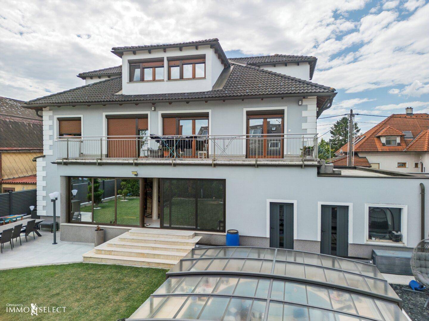 Rückseite des Hauses mit großem Garten, Terrasse und überdachtem Poolbereich, ideal für Entspannung.
