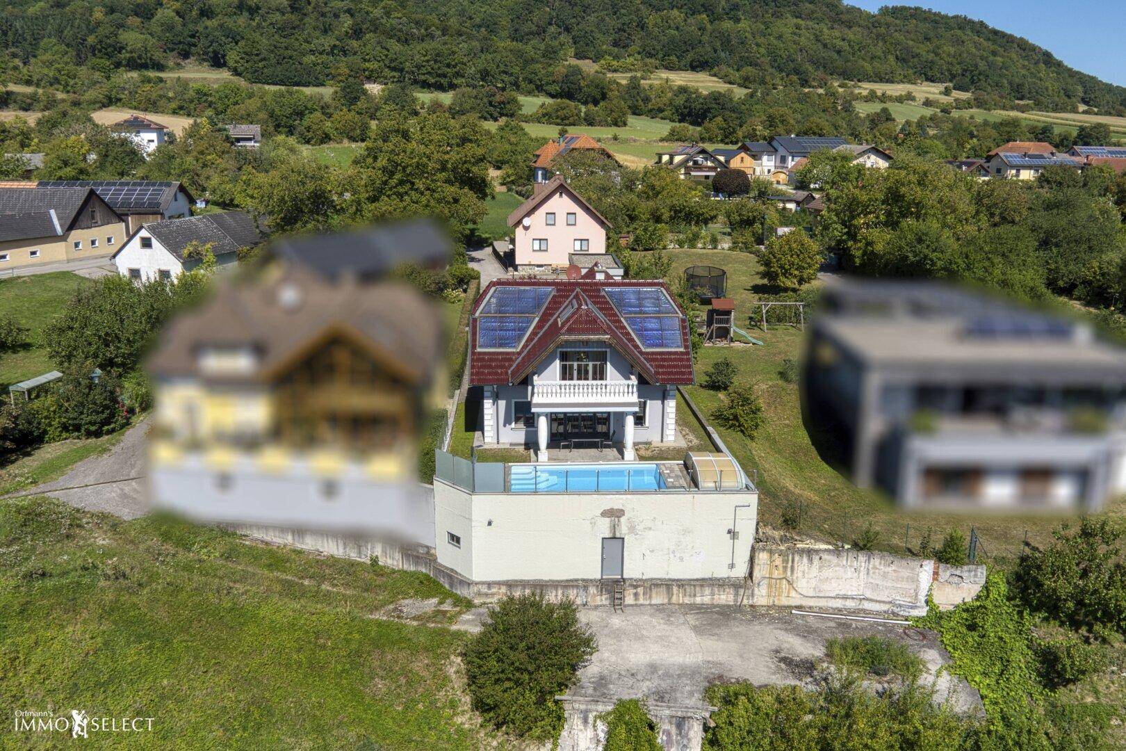 Luftaufnahme eines modernen Hauses mit Pool, Photovoltaikanlage und Bergblick.