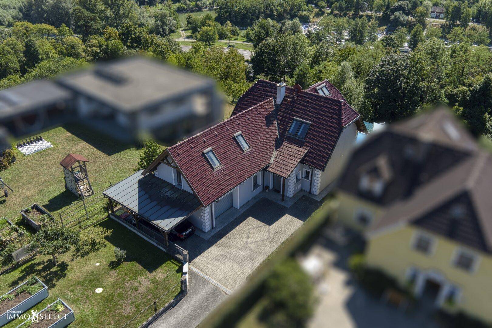 Luftaufnahme eines Einfamilienhauses mit rotem Ziegeldach, Carport und Gartenbereich.