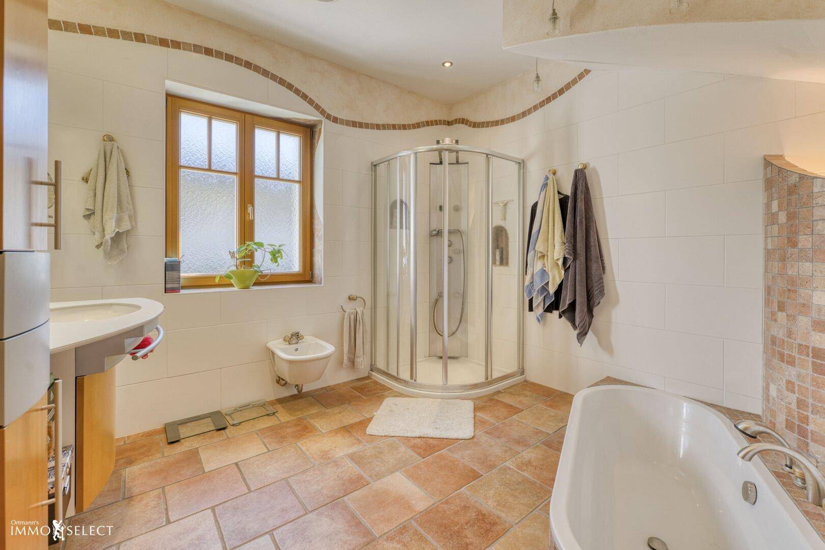 Geräumiges Badezimmer mit Terrakottafliesen, Badewanne, Dusche, Bidet und Fenster.
