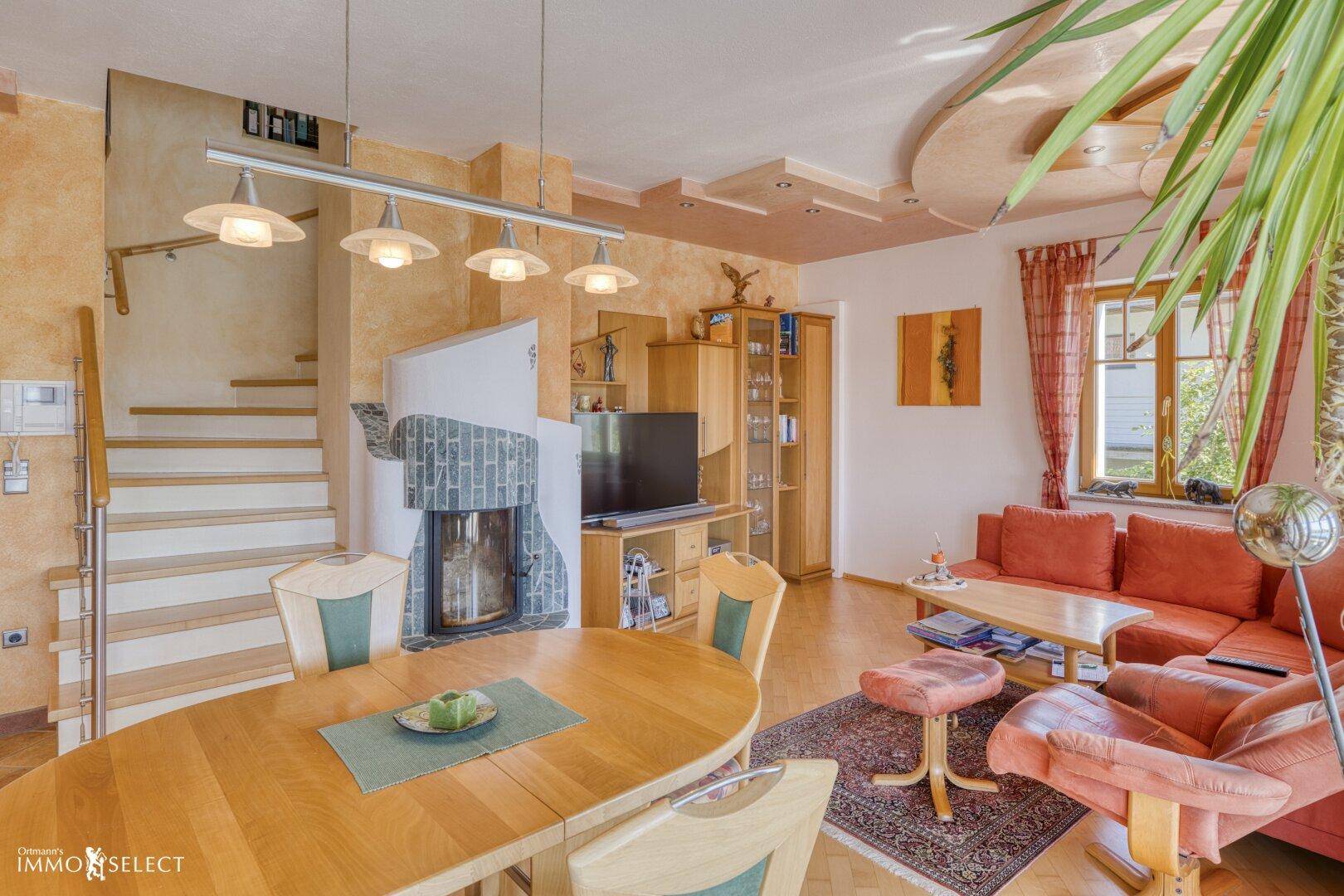 Geräumiger Wohn-Essbereich mit Kamin, Holztreppe und Blick auf die umliegende Landschaft.