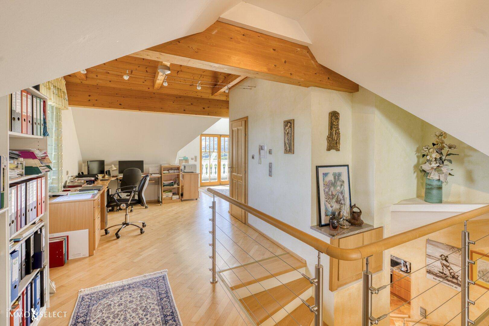 Helles Dachgeschoss-Büro mit Holzbalken, Parkettboden und Blick auf die umliegende Natur.