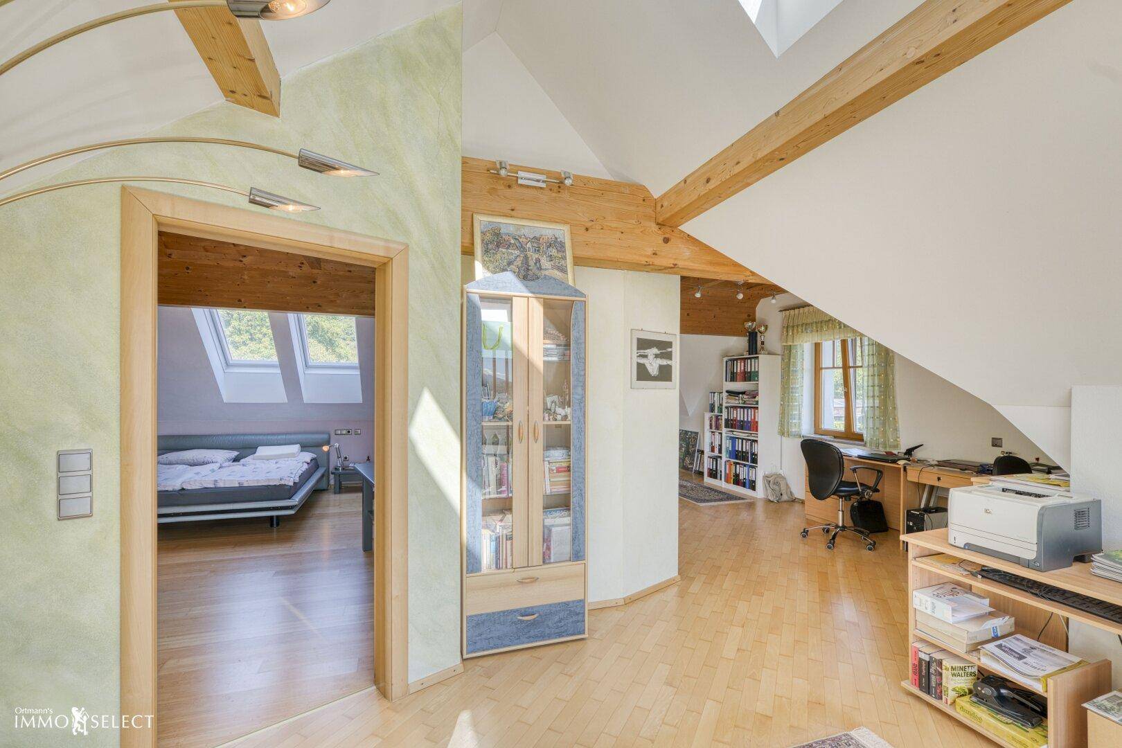 Offener Dachgeschossbereich mit Arbeitsplatz, Holzbalken und Zugang zum Schlafzimmer.