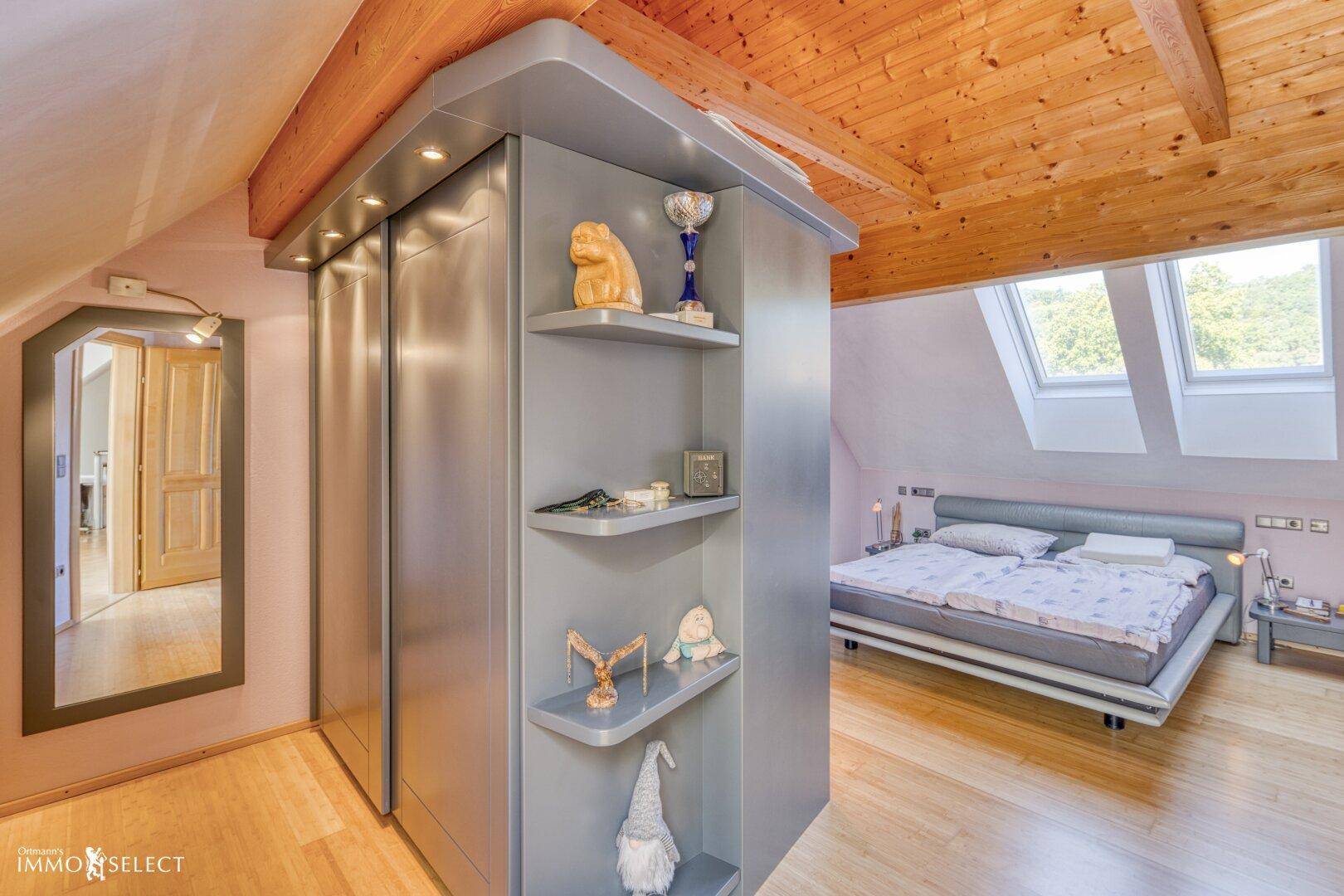 Gemütliches Schlafzimmer im Dachgeschoss mit Holzbalken, Dachfenstern und integriertem Kleiderschrank.