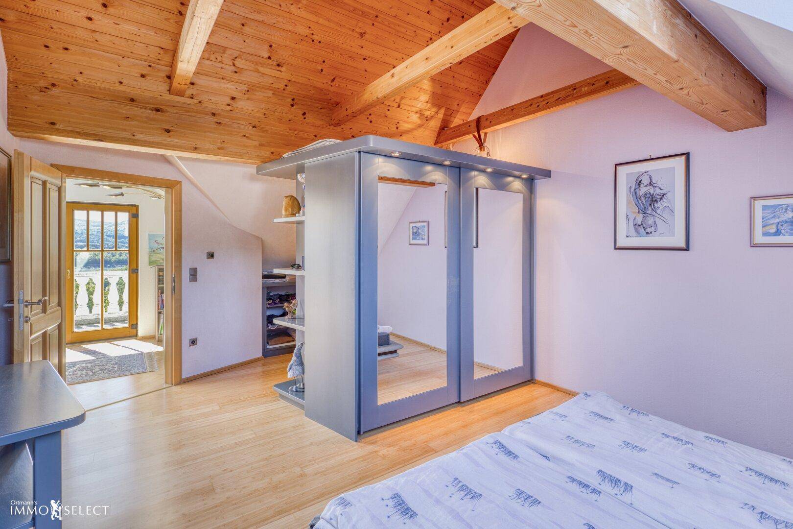Schlafzimmer im Dachgeschoss mit Holzbalkendecke, Parkettboden und Zugang zum Balkon.