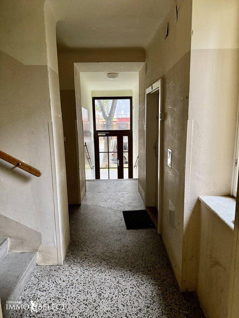 Heller Eingangsbereich eines Mehrfamilienhauses mit Terrazzoboden und Aufzug.