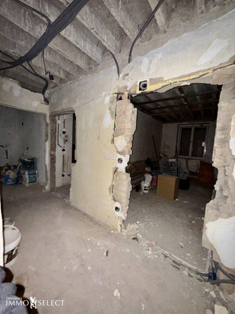 Renovierungsbedürftiger Raum mit freigelegten Ziegelwänden und Deckenbalken, bereit für den Ausbau.