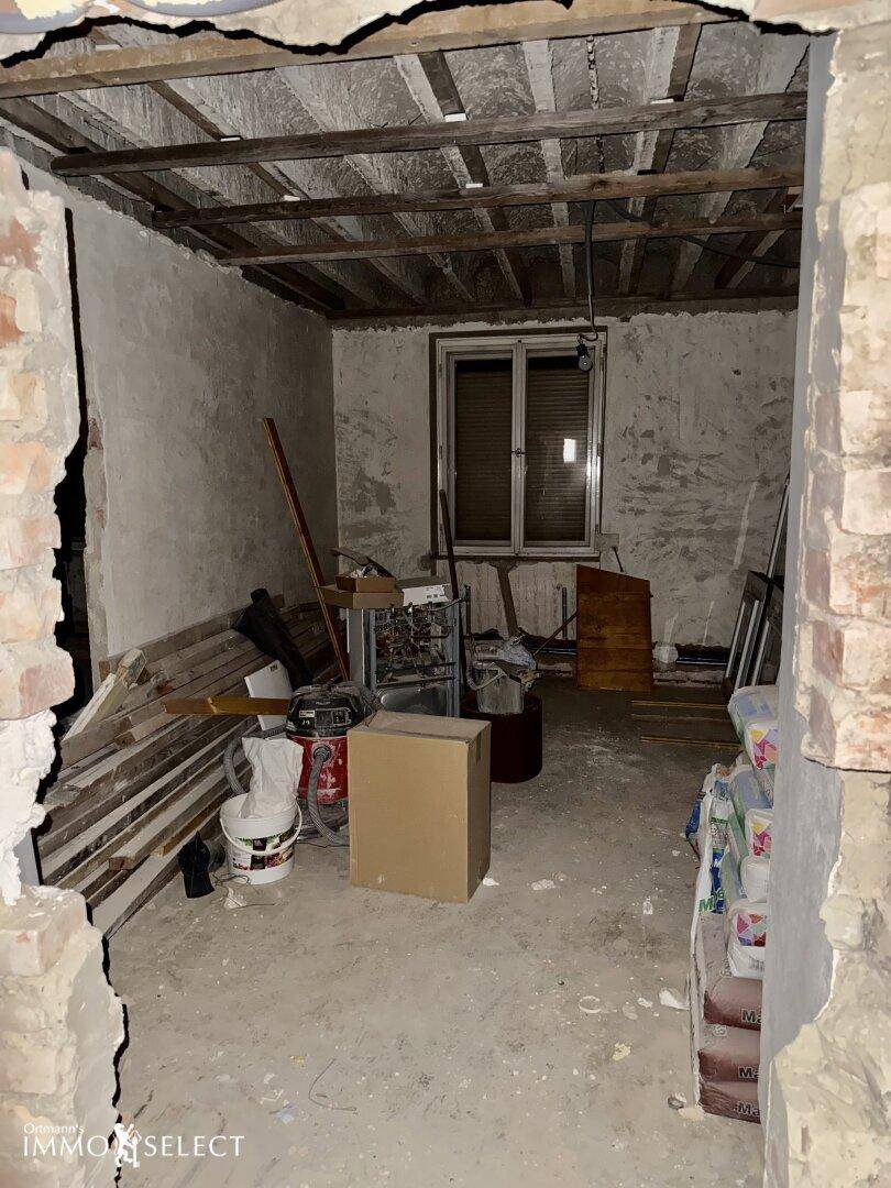 Renovierungsbedürftiger Raum mit Baumaterialien, freiliegender Decke und einem Fenster.