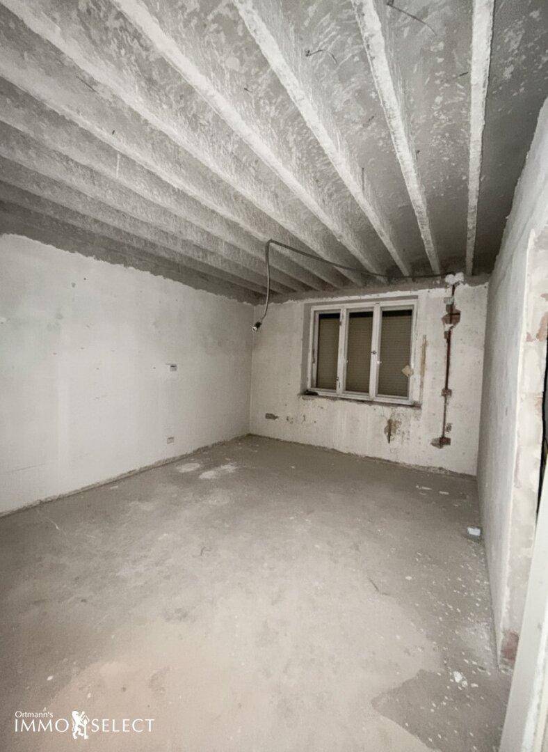 Renovierungsbedürftiger Raum mit Betonboden, freiliegender Decke und einem Fenster.